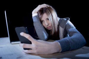 worried teenager using mobile phone and computer as internet cyb